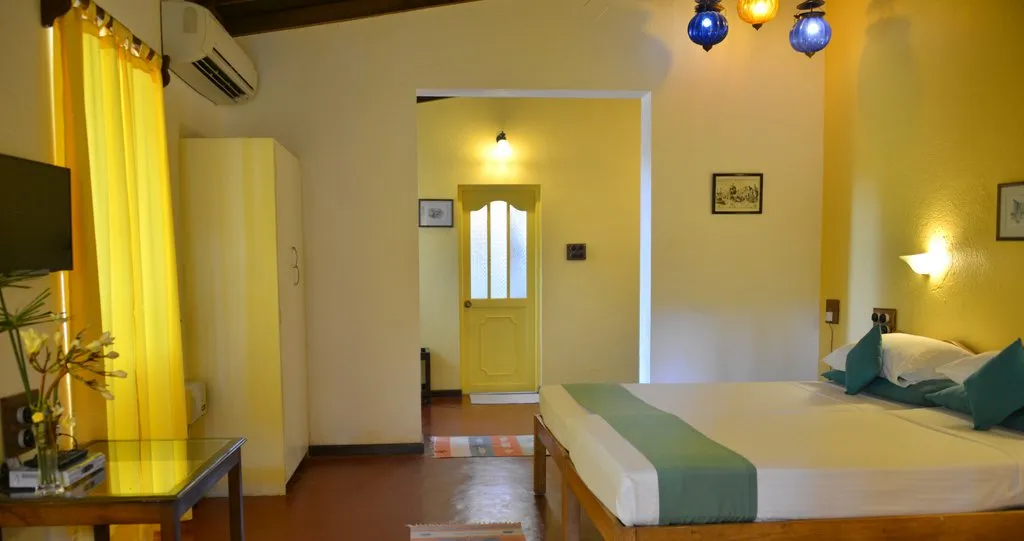 Twin beds with teal cushions against a sunny yellow wall at Cavala